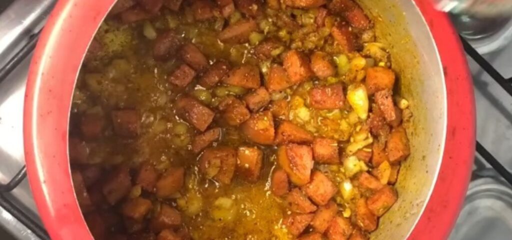 Linguiça picada com cebola e alho dentro de uma panela de pressão.